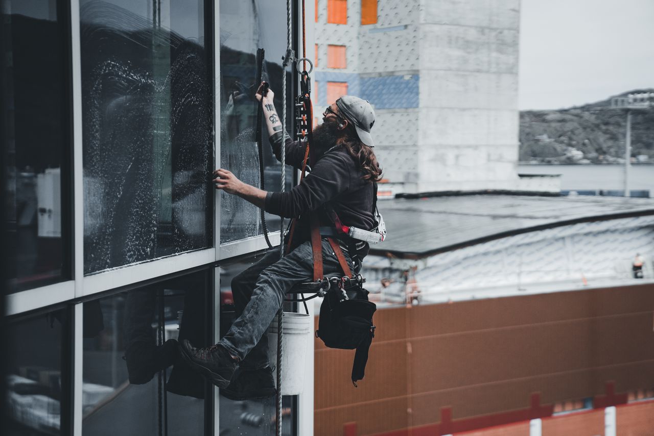 A worker washing the windows of a skyscraper while secured in a harness, highlighting high-rise urban maintenance work.